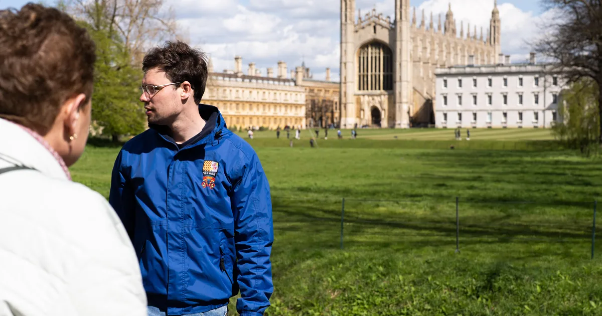 A student guide talking to visitors on the lawn in front of King's College Chapel in Cambridge